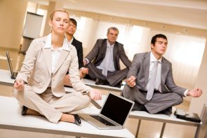 Portrait of meditating partners sitting on desks with their legs crossed in office